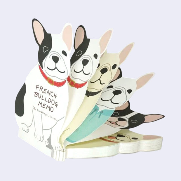 Die cut French bulldog memo pad, being leafed through to show 5 different sheets, each with different color dogs and some wearing different attire. All are smiling, though some with open mouths.