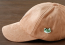 3D ceramic brooch/pin of a frog's head - green in coloring with 2 large eyes and a closed mouth, on a brown cap.