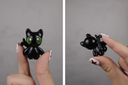 Black cat-shaped ceramic figure held by a hand against a gray background