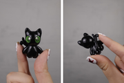 Black cat-shaped ceramic figure held by a hand against a gray background