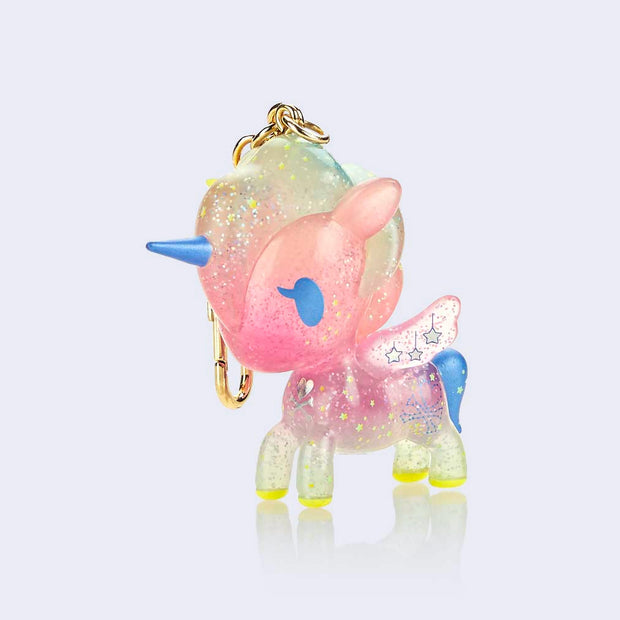 Semi transparent vinyl figure of a unicorn with glitter injection, primarily pink with blue and pink accents. Stars and moons decorate the figure, which is attached to a gold keychain.