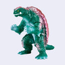A toy monster figure of Gamera with a green body, pink shell, and yellow eyes, shown against a plain light gray background.