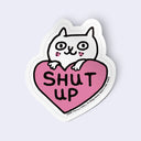 Sticker with a cat inside a heart-shaped 'SHUT UP' on a light gray background