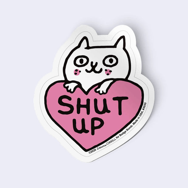 Sticker with a cat inside a heart-shaped 'SHUT UP' on a light gray background