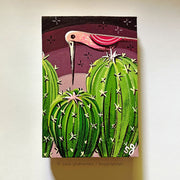 Illustrative painting of a pink bird with a long beak standing atop of rounded cacti, beak faced down. Background is a reddish purple sky.