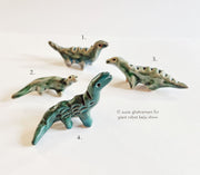 Set of 4 small green and blue ceramic dinosaurs. They are glazed and each have long necks and stand on 4 legs.