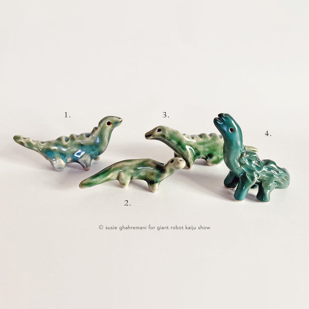 Set of 4 small green and blue ceramic dinosaurs. They are glazed and each have long necks and stand on 4 legs.