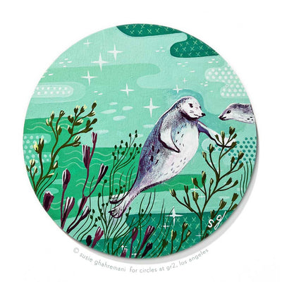 Painting on circular panel a fat seal, swimming in a seafoam green body of water with kelp and other sea plants reaching up towards it. A smaller seal swims slightly into the image area.