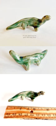 Small ceramic sculpture of a bluish green dinosaur with a long turned neck and round eyes.
