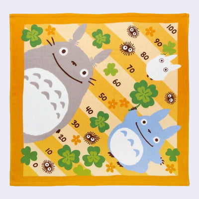 Square cloth featuring characters from My Neighbor Totoro, smiling in front of a chart of numbers, going in 10's from 0 to 100. Yellowy orange flowers and green clovers surround them.