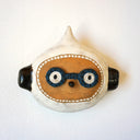 Ceramic sculpture of a tan animal like character's face with a small black nose on a tiny snout and wearing glasses and a white hood hat. 