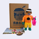 Colorful soft vinyl figure of an orange glittery man holding a pink fish in front of a cardboard box with a face design.