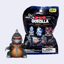 A Godzilla Sofvi Puppet Mascot 2 figure shown in front of its black retail packaging on a light gray background. The figure is dark gray with a red chest stripe and an orange-brown belly.