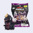 A Godzilla Sofvi Puppet Mascot blind bag toy set shown with the figure in front of its retail packaging. The figure is dark gray/black with a gold horn and a white crystal.