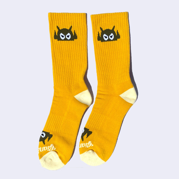 Goldenrod yellow socks with an olive green cartoon robot head on them and cream colored heels and toes. The robot head decorates the cuff end of each sock so that it peeks out when you wear sneakers.