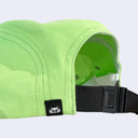 Close-up of a bright lime green baseball cap showing the side panel, black adjustable strap, plastic buckle, and a small black brand patch with a white stylized logo.