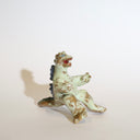 Ceramic sculpture of a sitting Godzilla, with its arms extended out as if for a hug. It has a variety of glazes, leaving it mostly a light mint green with brown undertones and speckles.