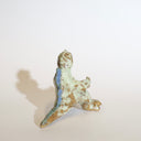 Ceramic sculpture of a sitting Godzilla, with its arms extended out as if for a hug. It has a variety of glazes, leaving it mostly a light mint green with brown undertones and speckles.