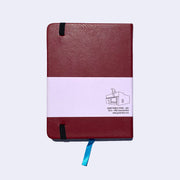 Backside of a burgundy red pleather covered journal with an elastic closure and a shiny blue page marking ribbon.