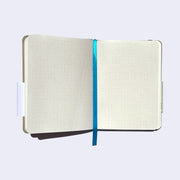 Interior of notebook, featuring cream colored pages with dots to mark space. A shiny blue place marking ribbon runs down the center.