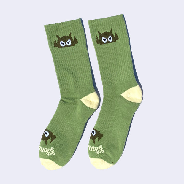 Green socks with a cartoon robot head on them and cream colored heels and toes. The robot head decorates the cuff end of each sock so that it peeks out when you wear sneakers.