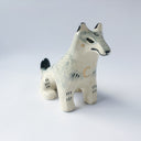 Cream colored ceramic sculpture of a sitting wolf, with subtle grayish blue coloring for its fur and black tail tip and back of its ears.