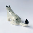 Cream colored ceramic sculpture of a sitting wolf, with subtle grayish blue coloring for its fur and black tail tip and back of its ears.