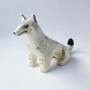 Cream colored ceramic sculpture of a sitting wolf, with subtle grayish blue coloring for its fur and black tail tip and back of its ears.