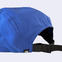 Close-up of the back of a royal blue baseball cap with a black adjustable strap and a small black brand tag featuring a white cat logo.