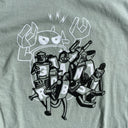 Light sage green t-shirt featuring a black and white illustration on the front. Many robots stumble over each other and march in the same direction. Letters on their stomachs spell "Giant Robot." Behind them, is a large white outlined Big Boss Robot, seemingly commanding them.