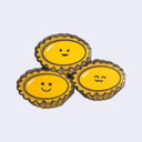 Three small yellow tart or pie-shaped enamel pins with simple black face details, arranged together on a light gray background.