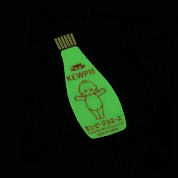 Die cut enamel pin of a bottle of Kewpie Mayonnaise glowing in the dark.