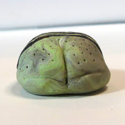 Small marbled green clay sculpture of a frog with a very pudgy body and a black triangle on its forehead. It sits with its arms and legs pulled in.