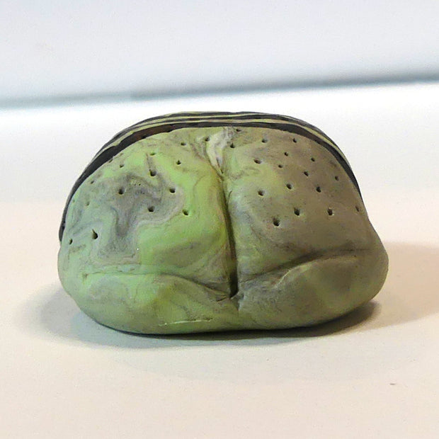 Small marbled green clay sculpture of a frog with a very pudgy body and a black triangle on its forehead. It sits with its arms and legs pulled in.