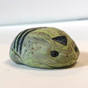 Small marbled green clay sculpture of a frog with a very pudgy body and a black triangle on its forehead. It sits with its arms and legs pulled in.