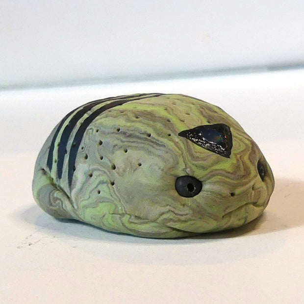 Small marbled green clay sculpture of a frog with a very pudgy body and a black triangle on its forehead. It sits with its arms and legs pulled in.