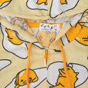 Light yellow hooded jacket with a repeating all over pattern of Gudetama, sitting on egg yolk, inside of an egg shell or wrapped in bacon. Close up.
