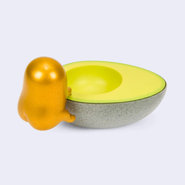 Back view of Gudetama figure, metallic gold and climbing up into a half of an avocado. Its butt cheeks are pronounced. 