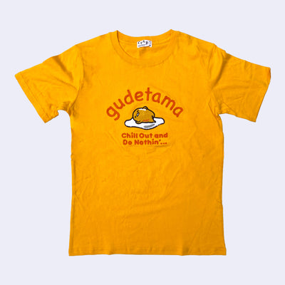 Golden yellow t-shirt featuring a tufted embroidery of Sanrio's Gudetama, laying on his egg white. Above him reads "gudetama" and below "chill out and do nothin'..."