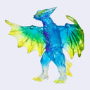 A translucent dragon figurine or toy with a blue body and wings that fade into yellow and green, shown against a plain light gray background.