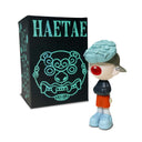 Painted resin figure of a boy with a backwards cap, ear piercings and baggy clothing. He has an open mouth with only one tooth and most of his face is obscured by a blue demon mask.