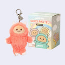 Plush charm of a pastel red Yeti character with a keychain attachment next to its packaging.
