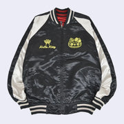Black satin jacket with white side detailing and a gold graphic of Hello Kitty's head in a Day of the Dead skull pattern design. On the other side of the lapel is a gold butterfly and underneath cursive "Hello Kitty"