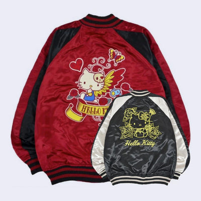 Red satin jacket with black side detailing and with a large embroidered graphic of Hello Kitty on the back, sitting with a skull hair clip and butterfly wings. Below is a banner that says "Hello Kitty". The jacket is reversible, with a black and white satin option on the other side with gold line art of Hello Kitty.