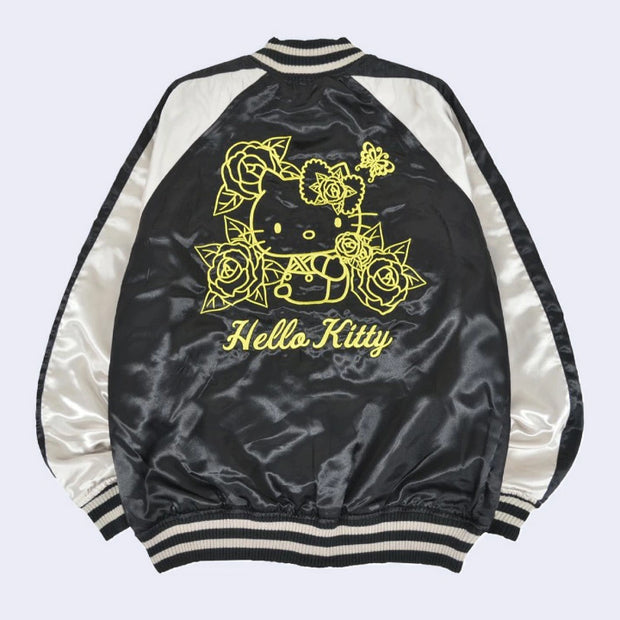Backside of a black satin jacket with white side detailing. It has gold embroidered line art of Hello Kitty sitting with roses around her and a butterfly overhead. Below her is cursive writing "Hello Kitty".