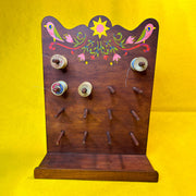 Wooden thread holder, with many pegs to hold many spools of thread, with a retro style pattern painted atop it of 2 pink birds and florals.