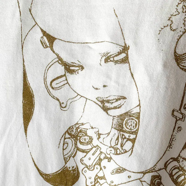 White shirt with a line art illustration in the center of a woman with many mechanical head and body elements. Line art is in a dark gold color. Close up.