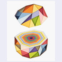 Two colorful geometric cut paper art pieces on a white background. The bottom has an exposed cross section with many layers and the top piece seems to be lifted from the whole.