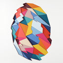 Colorful cut paper pieces puzzled into and atop of one another to create a geometric shaped ball with slightly jagged edges. White paper surrounds the enclosed shapes.