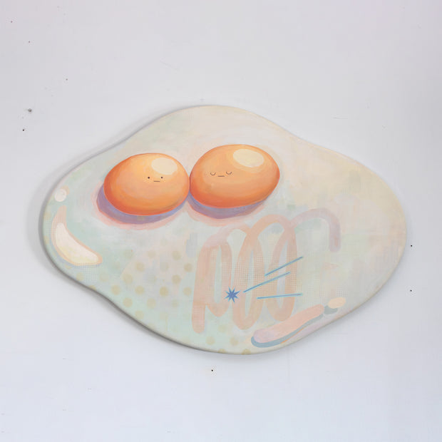 Die cut canvas of a pair of 2 eggs sharing a single egg white. The yolks are touching and have small faces. The egg white contains a subtle polka dot and scribble design.